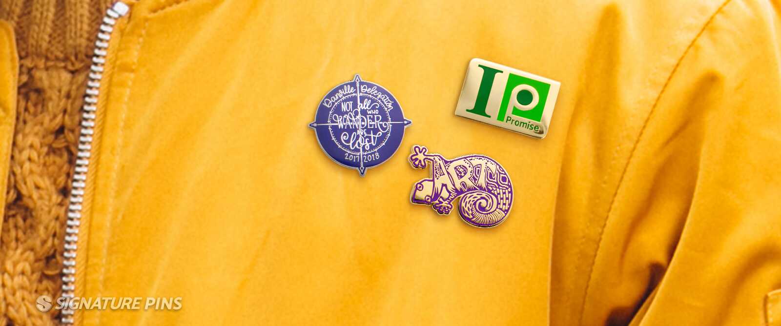 Three cloisonné pins on a yellow jacket: Danville Delegation compass with Not All Who Wander Are Lost, IP Promise logo, and purple chameleon ARC pin