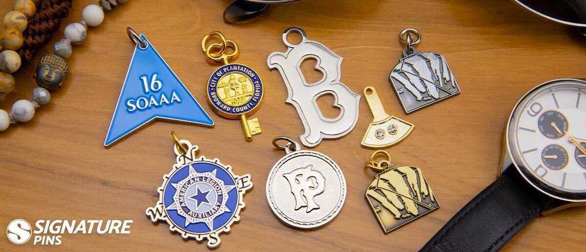 Assorted custom charms on wooden surface including pennant, key, letter, and compass designs in gold and silver