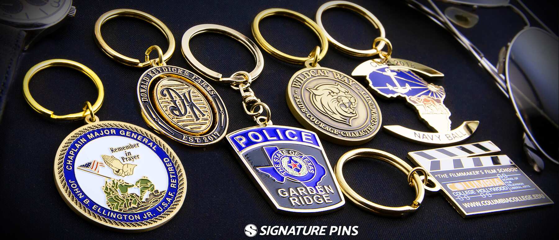 Assorted custom keychains including military, police badge, Navy Ball anchor, and film school clapperboard designs