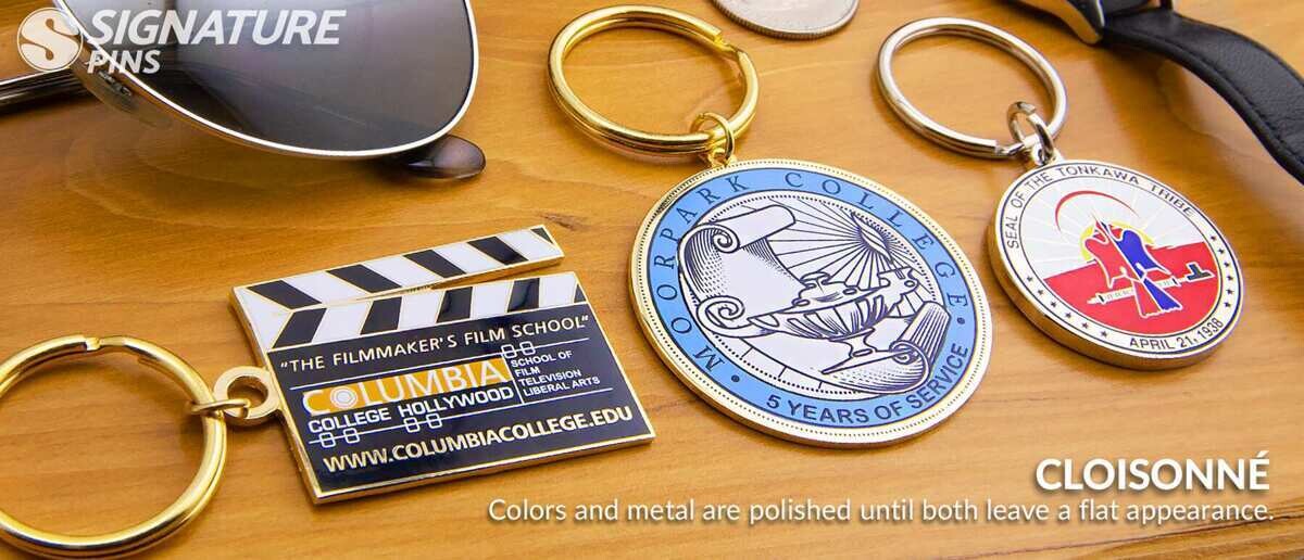 Cloisonne keychains including film school clapperboard, college service award, and tribal seal designs
