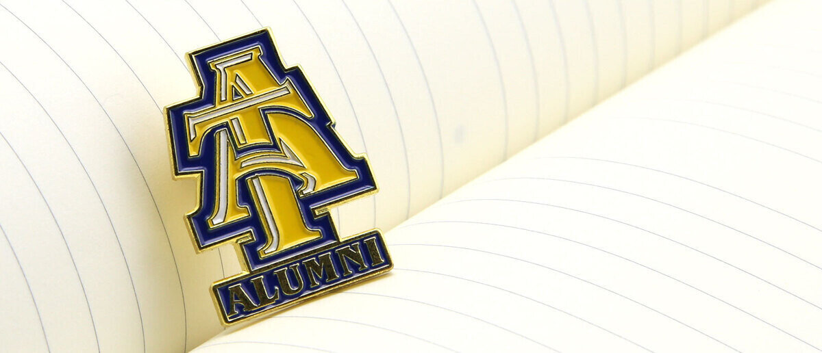 Blue and gold interlocking AT alumni pin on lined notebook