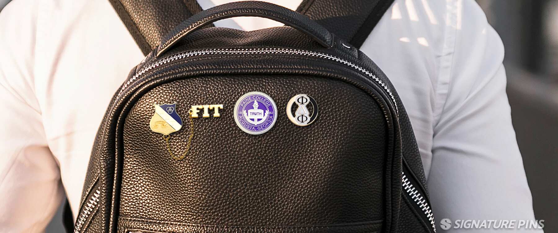 Black leather backpack with FIT, college seal, and Greek letter fraternity pins