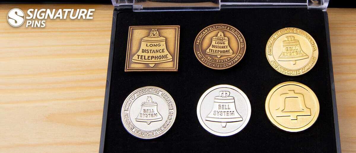Bell System telephone pins displayed in various metal plating finishes including antique bronze, silver, and high polish gold