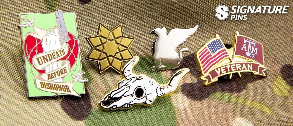Military hat pins on camouflage including Texas A&M Veteran, eagle, and Undeath Before Dishonor designs