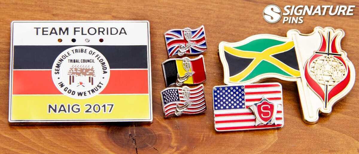 Collection of flag pins in various sizes including Team Florida Seminole Tribe NAIG 2017 pin, British flag, Belgian flag, American flag, and Jamaican flag pins