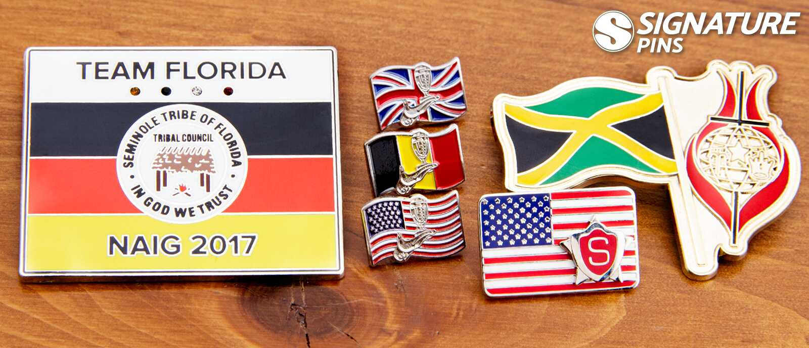 Collection of flag pins in various sizes including Team Florida Seminole Tribe NAIG 2017 pin, British flag, Belgian flag, American flag, and Jamaican flag pins