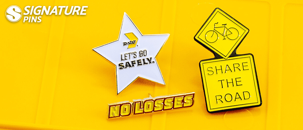 Collection of safety award pins including a silver star-shaped Let's Go Safely pin, yellow No Losses pin, bicycle Share the Road sign pin, and yellow caution sign pin