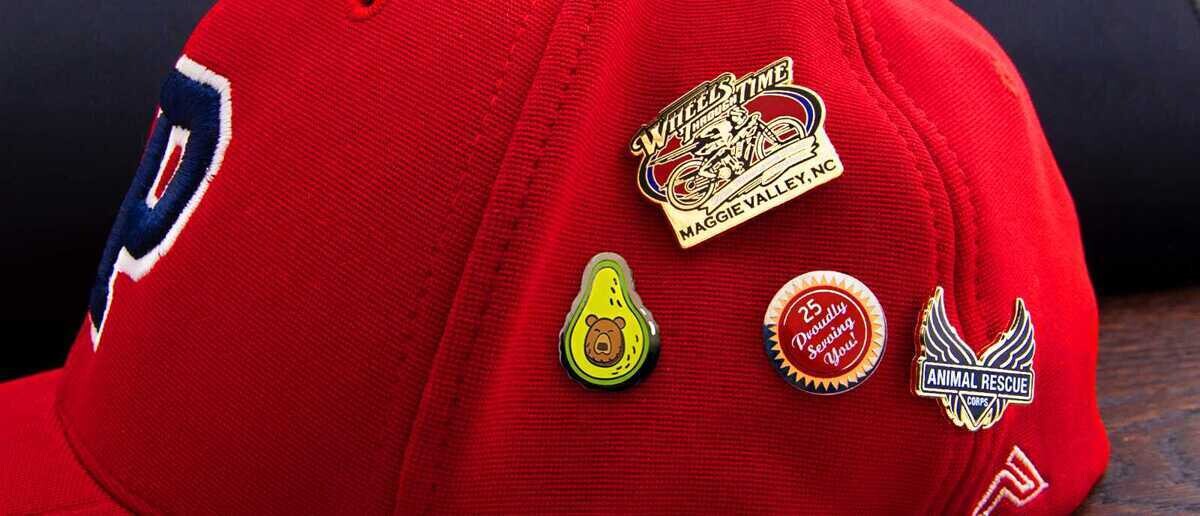 Red baseball cap with silkscreen pins including Wheels Time motorcycle, avocado bear, and Animal Rescue Corps
