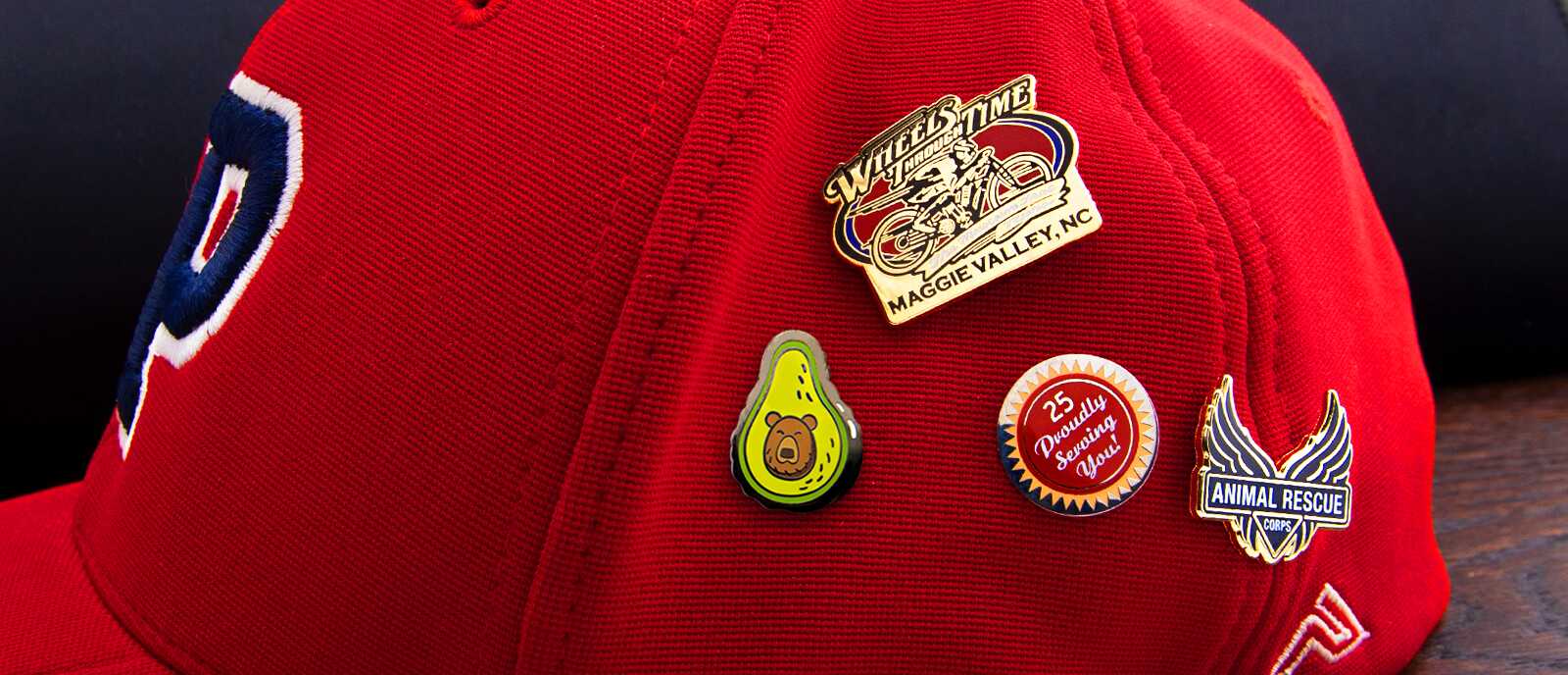 Red baseball cap with silkscreen pins including Wheels Time motorcycle, avocado bear, and Animal Rescue Corps