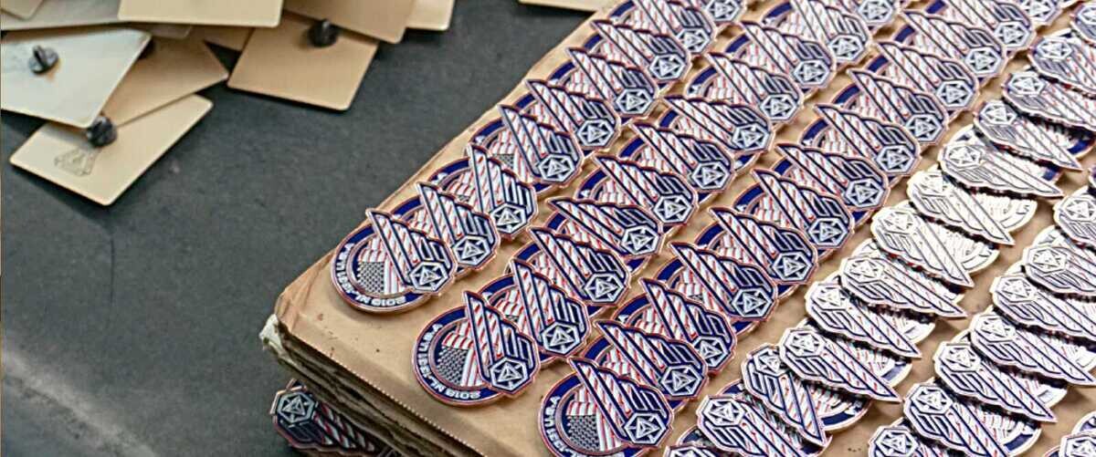 Hundreds of custom patriotic enamel pins arranged in rows during bulk order production