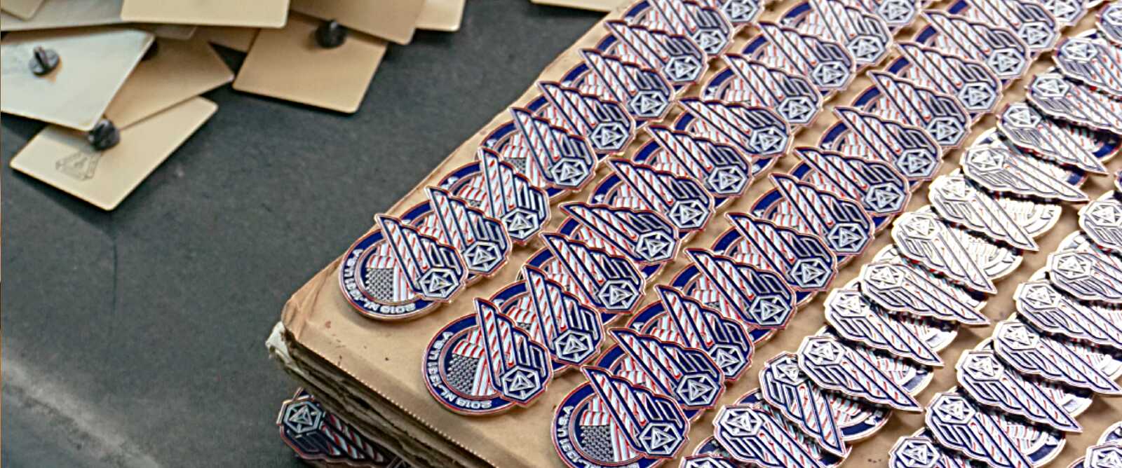 Hundreds of custom patriotic enamel pins arranged in rows during bulk order production